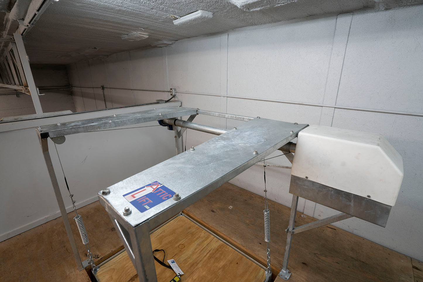 Attic lift installed in ceiling with visible motor housing and galvanized frame