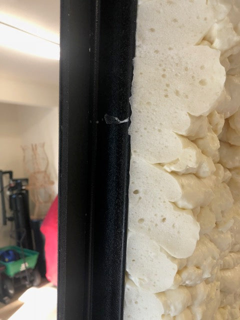 Close-up of attic lift insulation showing dense foam and black rubber weather stripping along the edge
